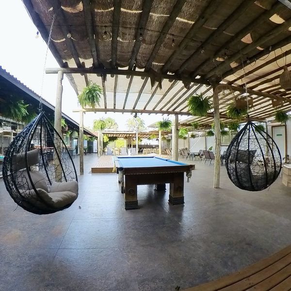 Mesa de sinuca e cadeiras-ovo suspensas no pátio coberto